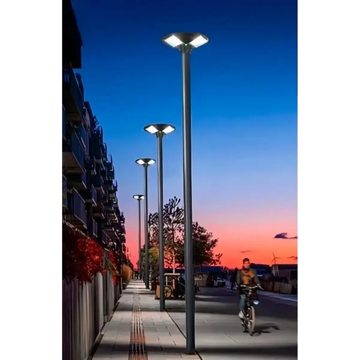 Fila de postes de luz de diseño moderno de ORBE - Postes Metalicos, con luminarias LED circulares de 360 grados, instalados en una ciclovía junto a un edificio al atardecer.