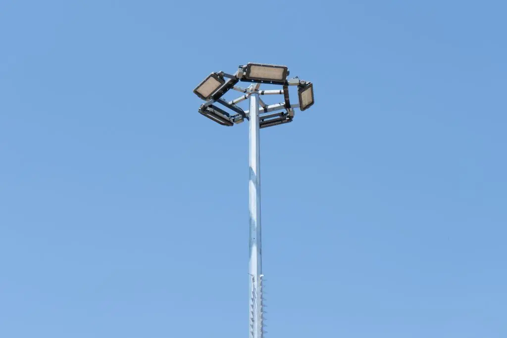 Poste metálico alto de ORBE - Postes Metalicos con luminarias LED de gran potencia en la parte superior, ideal para alumbrado de estadios, puertos y grandes espacios abiertos bajo un cielo azul claro.